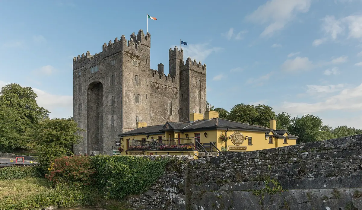 Il torrione merlato di Bunratty Castle con la bandiera irlandese e il vecchio ponte di pietra sul fiume