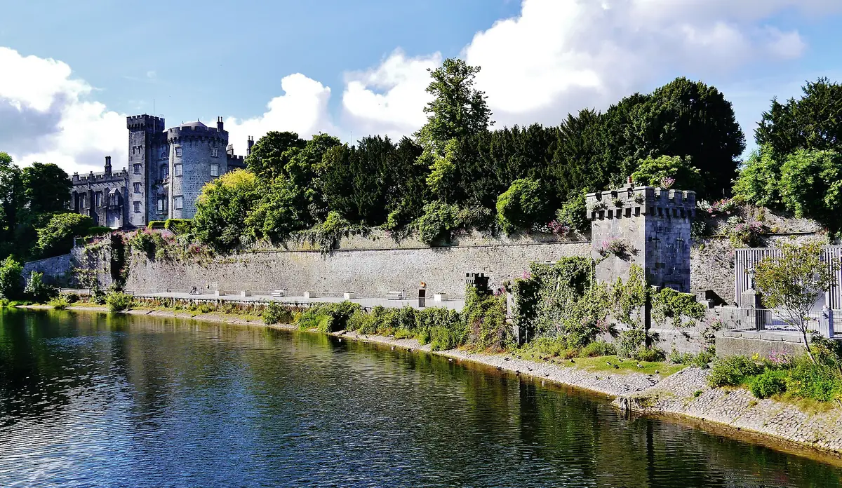 Kilkenny Castle con le sue torri tra gli alberi, sopra le mura di pietra lungo il fiume Nore